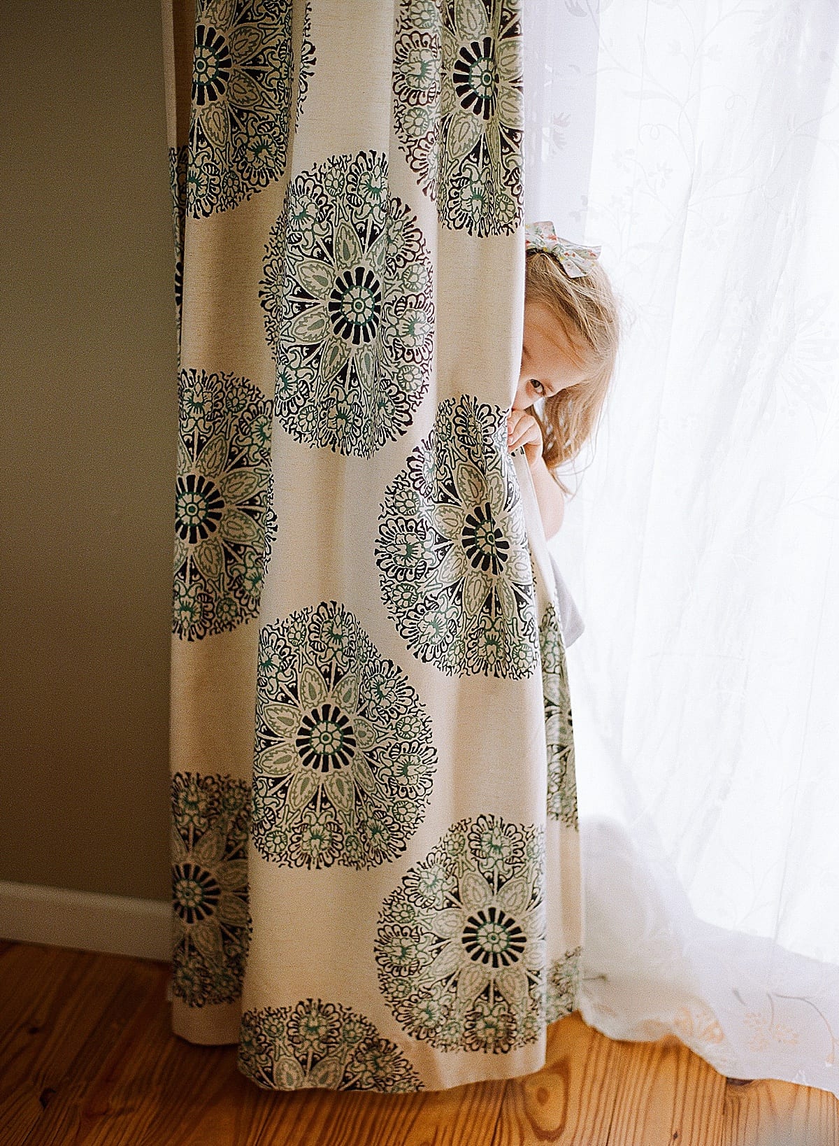 little girl peeking from behind the curtain photo