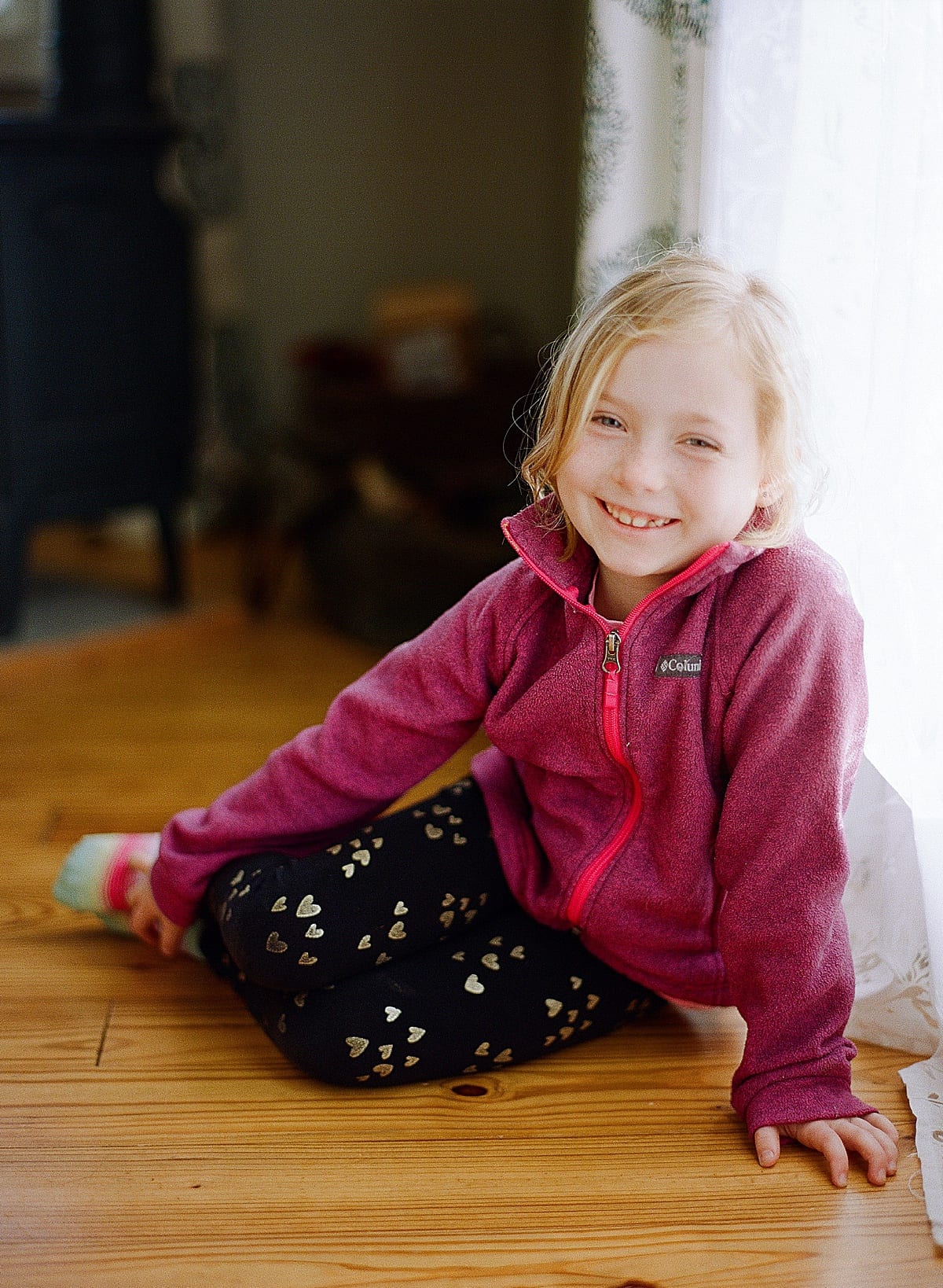 Little girl sitting by window smiling at camera photo 