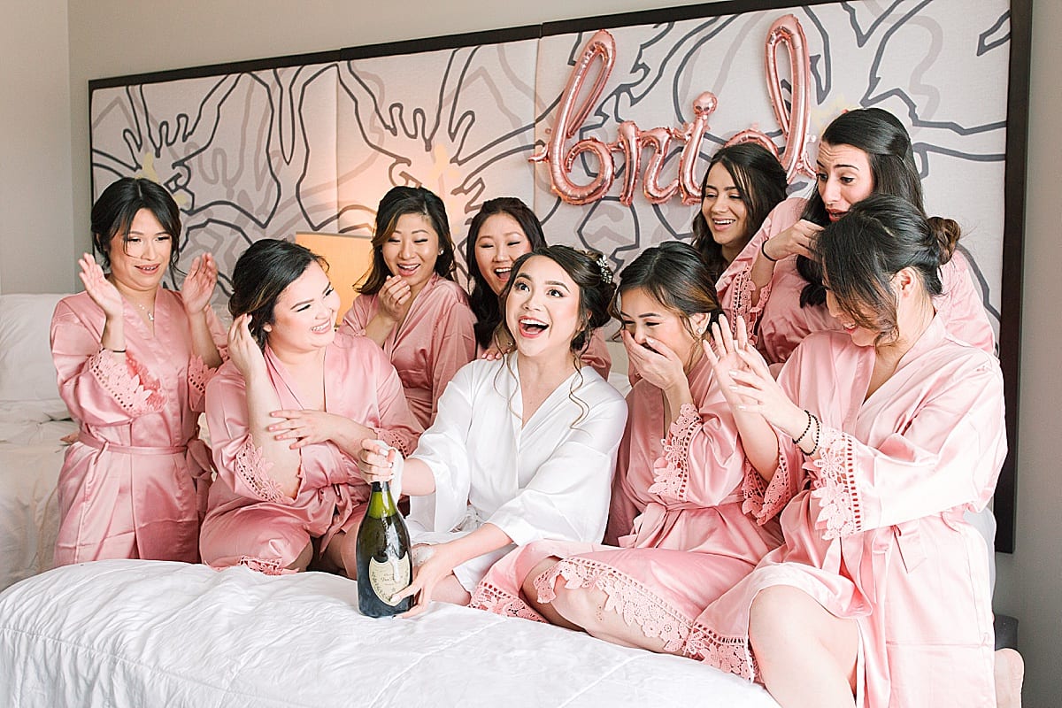 Bride Popping Champagne on bed with Bridesmaids Photo