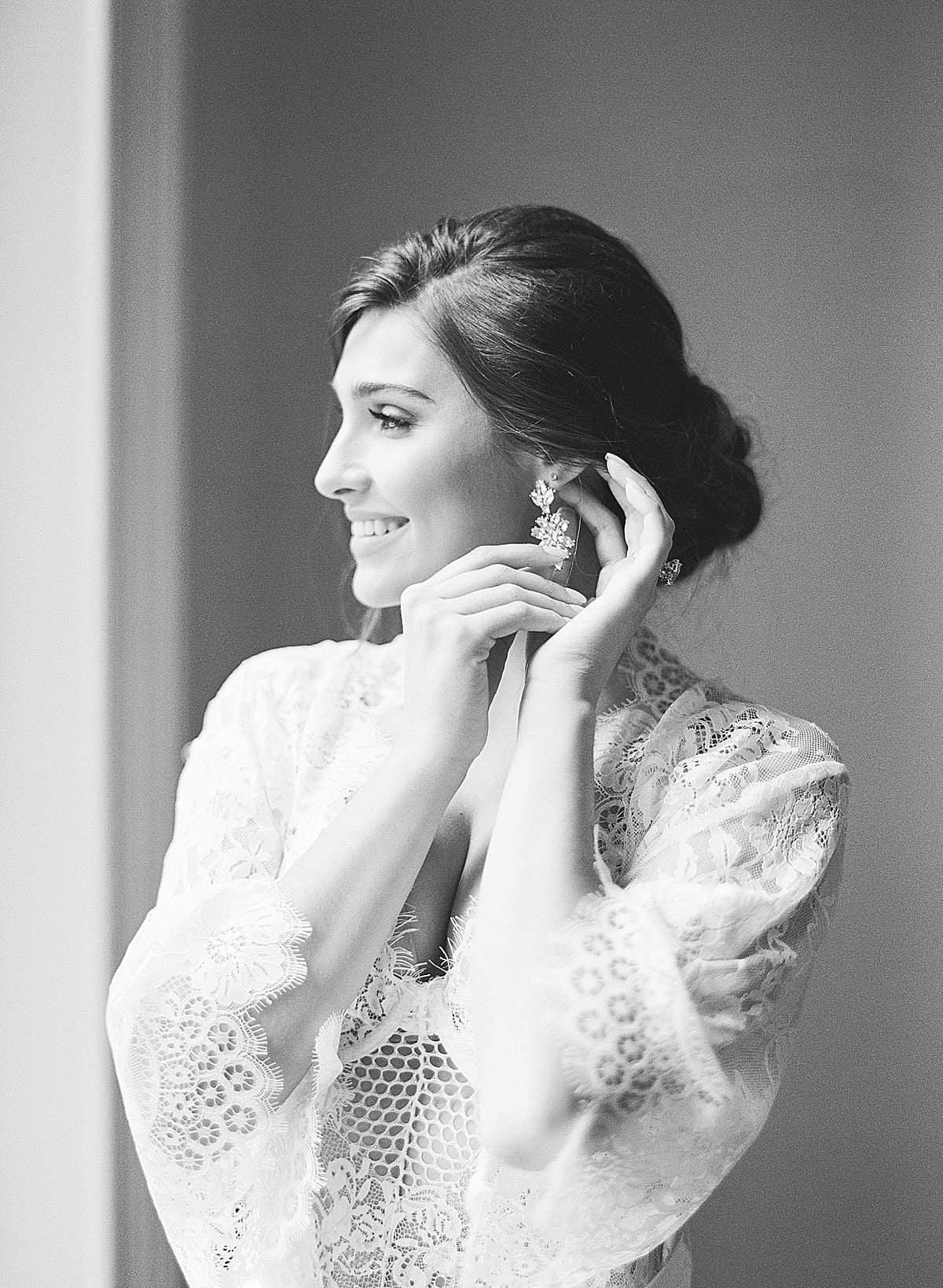 Boudoir Ideas Black and White of Bride Putting On Earring and Looking out Window Photo