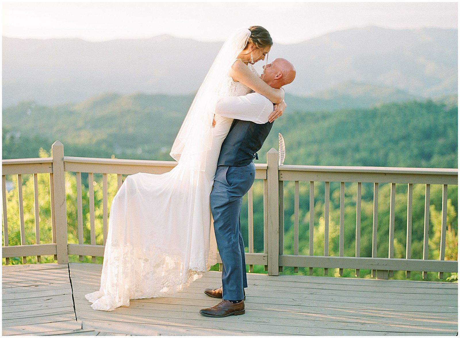 Groom Picking Bride Up With Mountains In Background Photo
