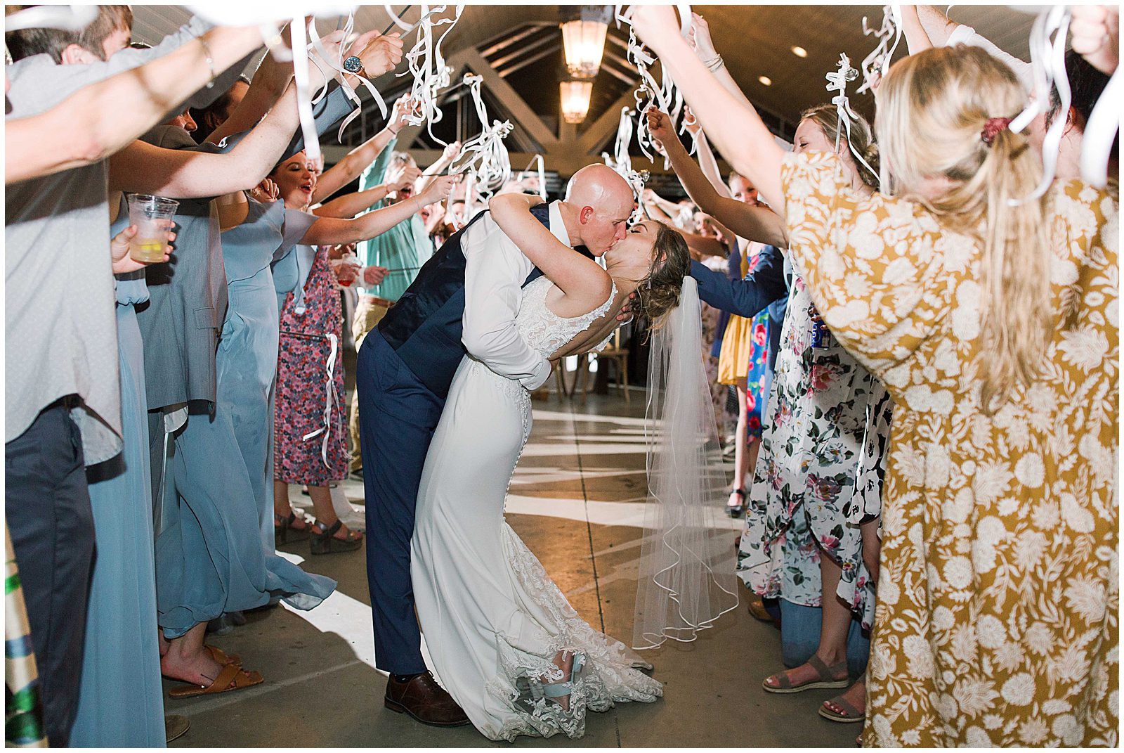 Couple Kissing While Guests Wave White Ribbon Wands Photo