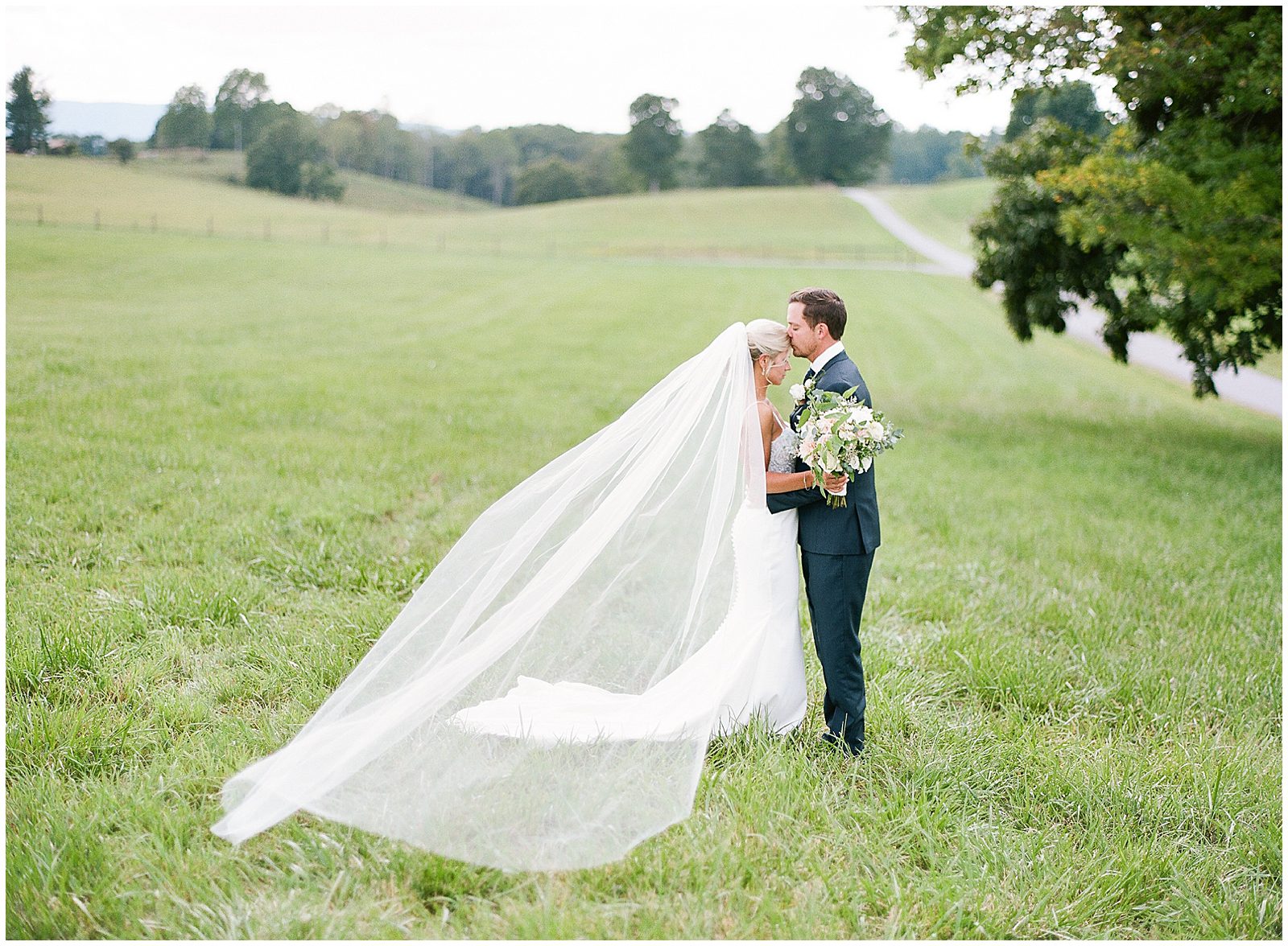 Bride and Groom in Field With Veil Blowing Photo
