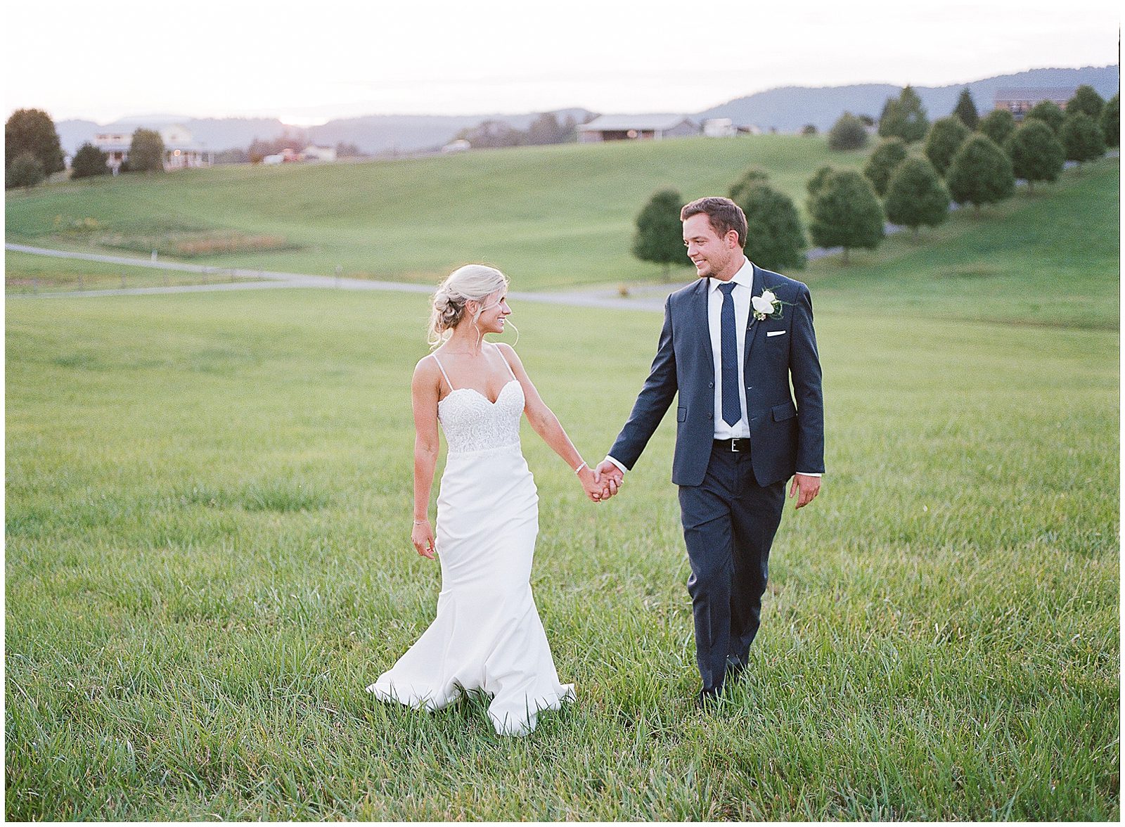 Bride and Groom Walking in Field Holding Hands Photo