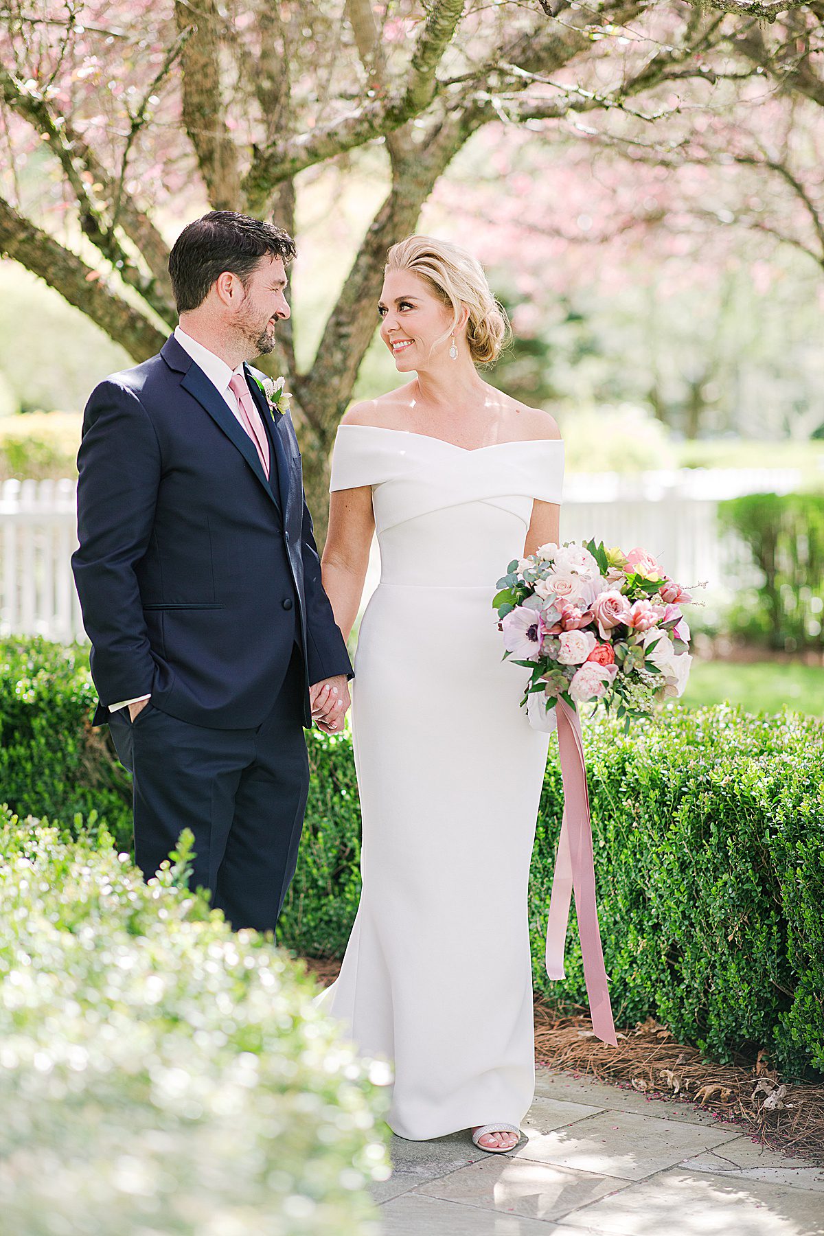 Bride in Romona Keveža Wedding Gown Walking with Groom in Garden Photo