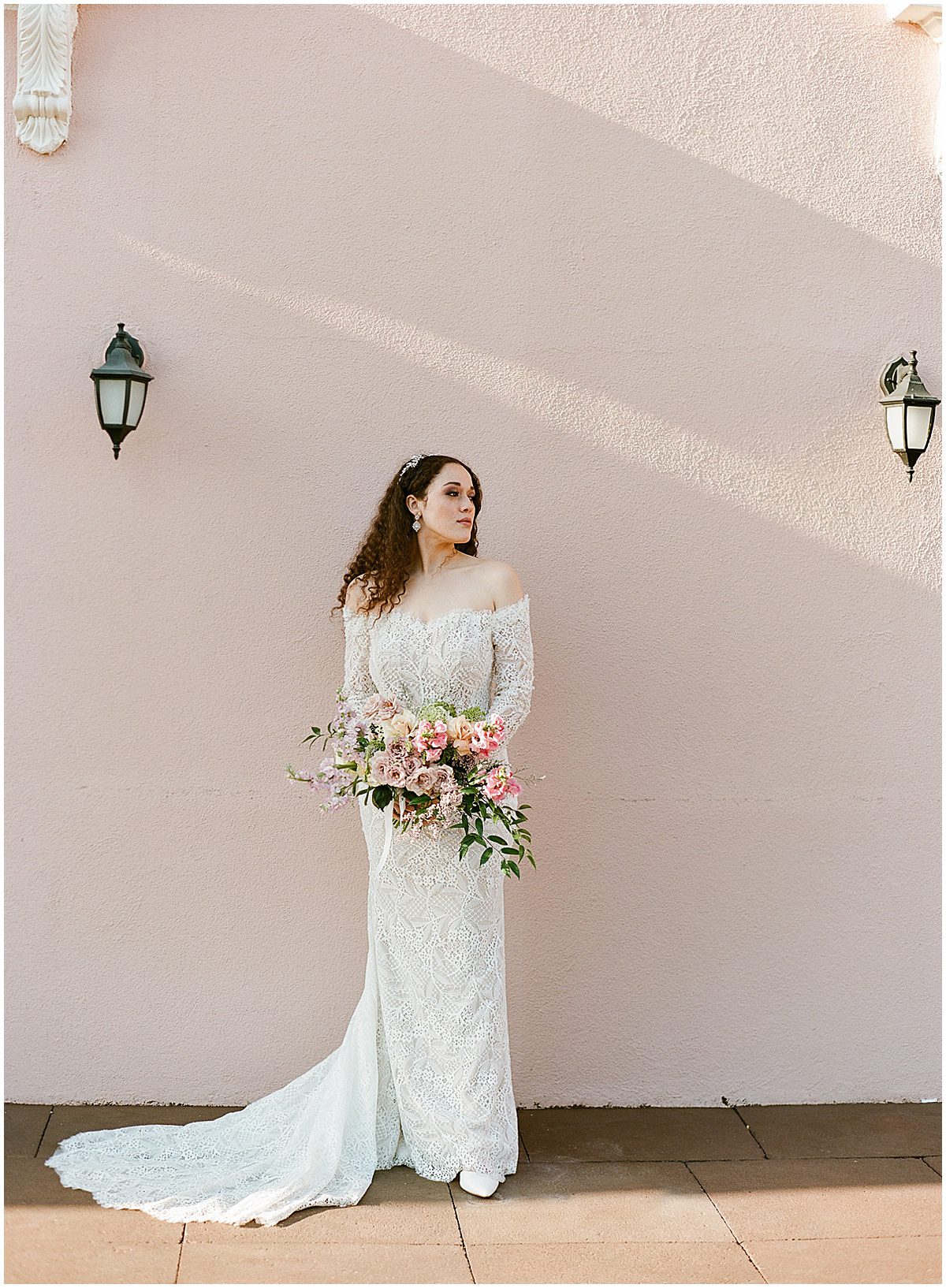 Bride in Lace Dress Holding Bouquet In Front of Pink Wall Photo
