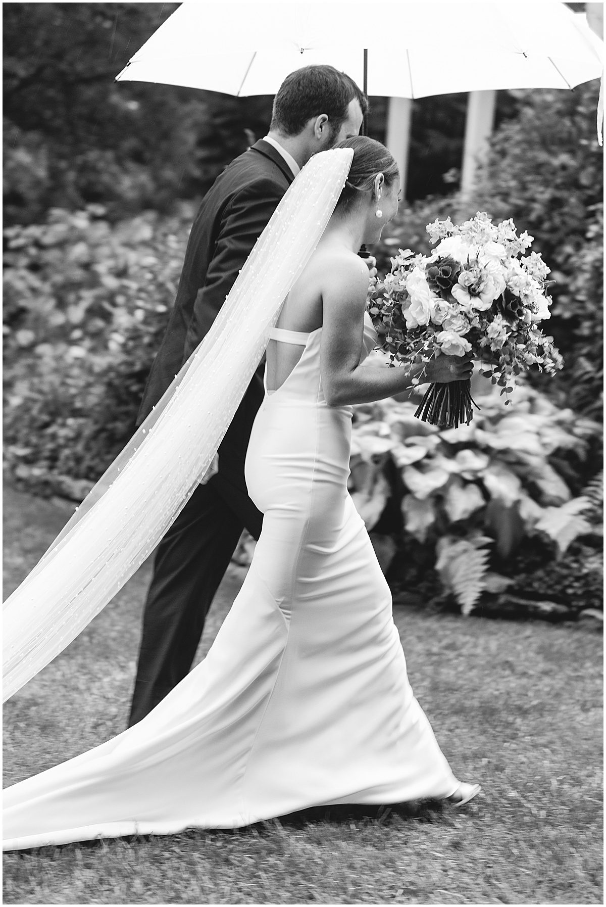 Black and White of Bride and Groom Walking Under Umbrella Photo