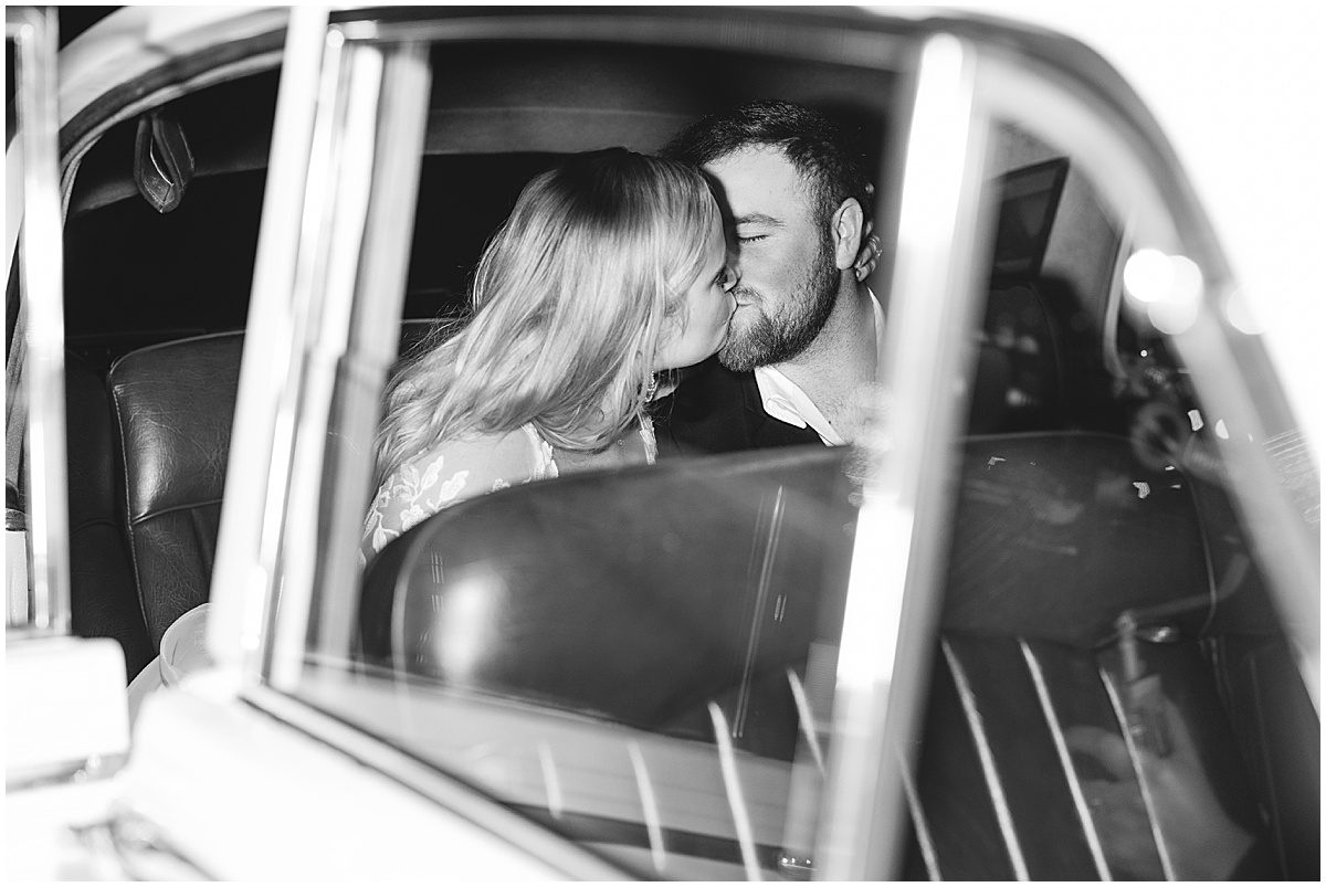 Black and White of Bride and Groom Kissing in Back of Vintage Car Photo