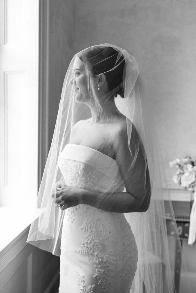 Bride looking out window with veil over her face photo