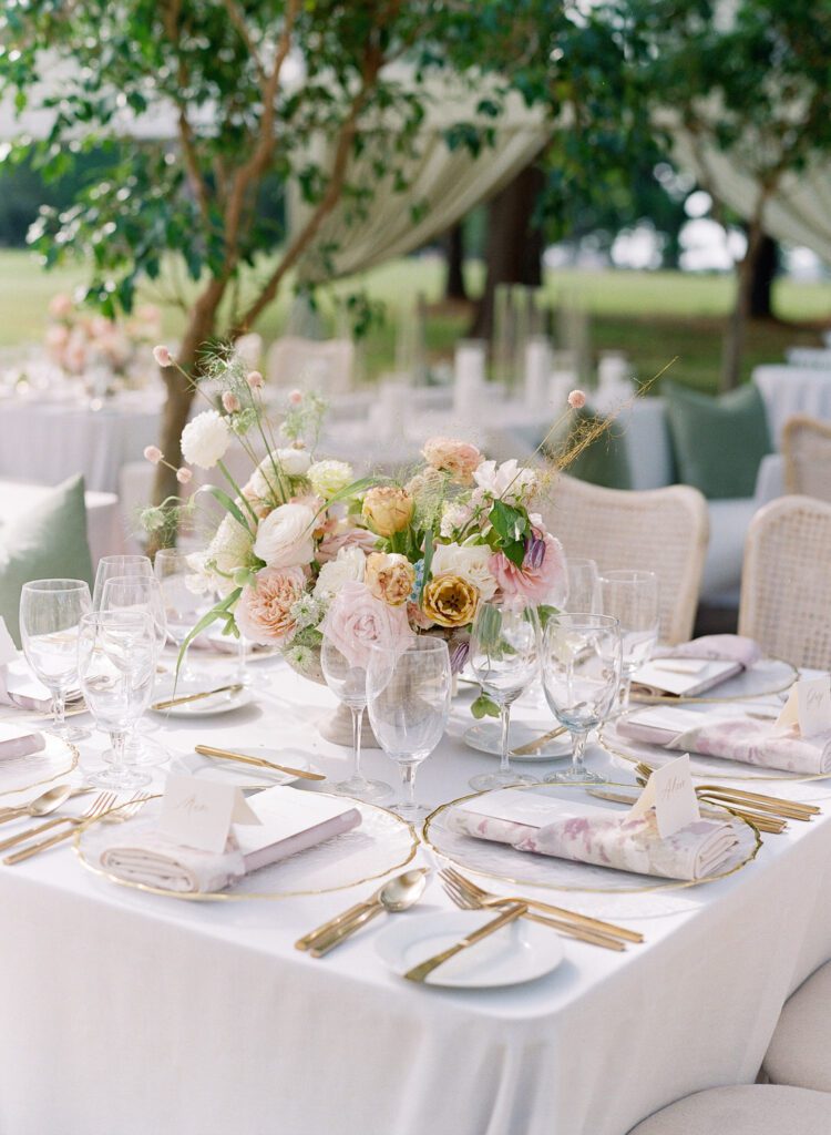 Wedding reception table setting with gold silverware and a pastel floral arrangement