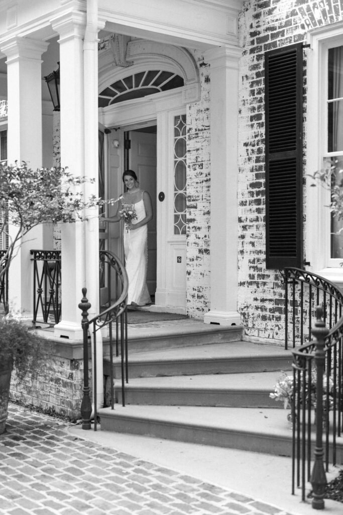 black and white of bride coming out of house 