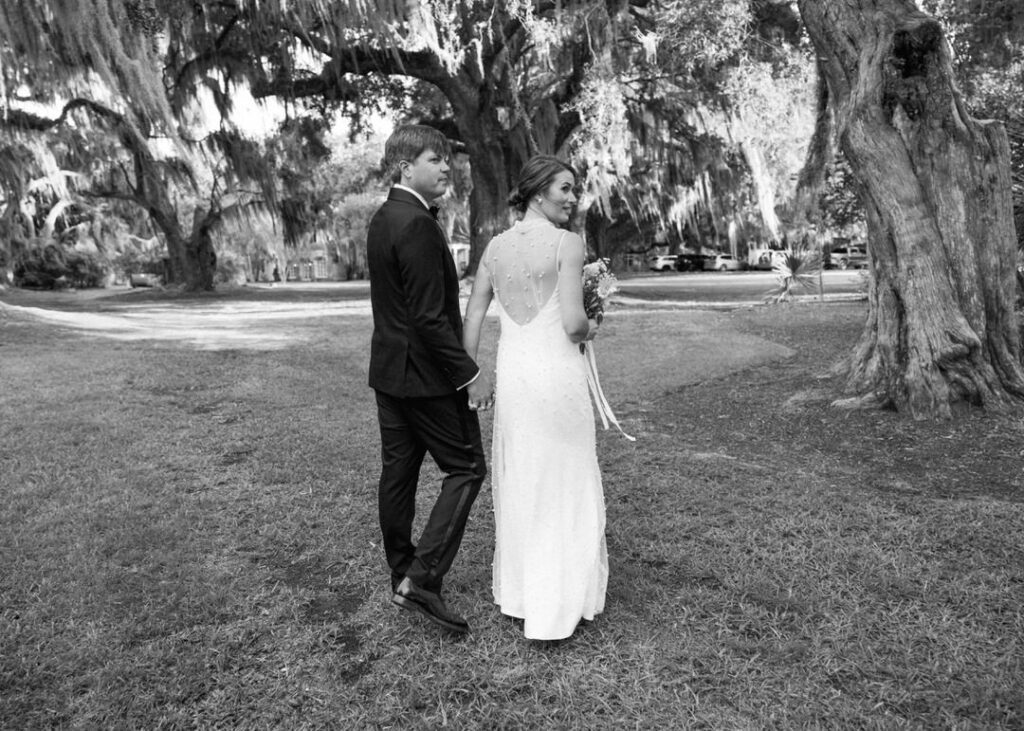 black and white of bride and groom walking holding hands