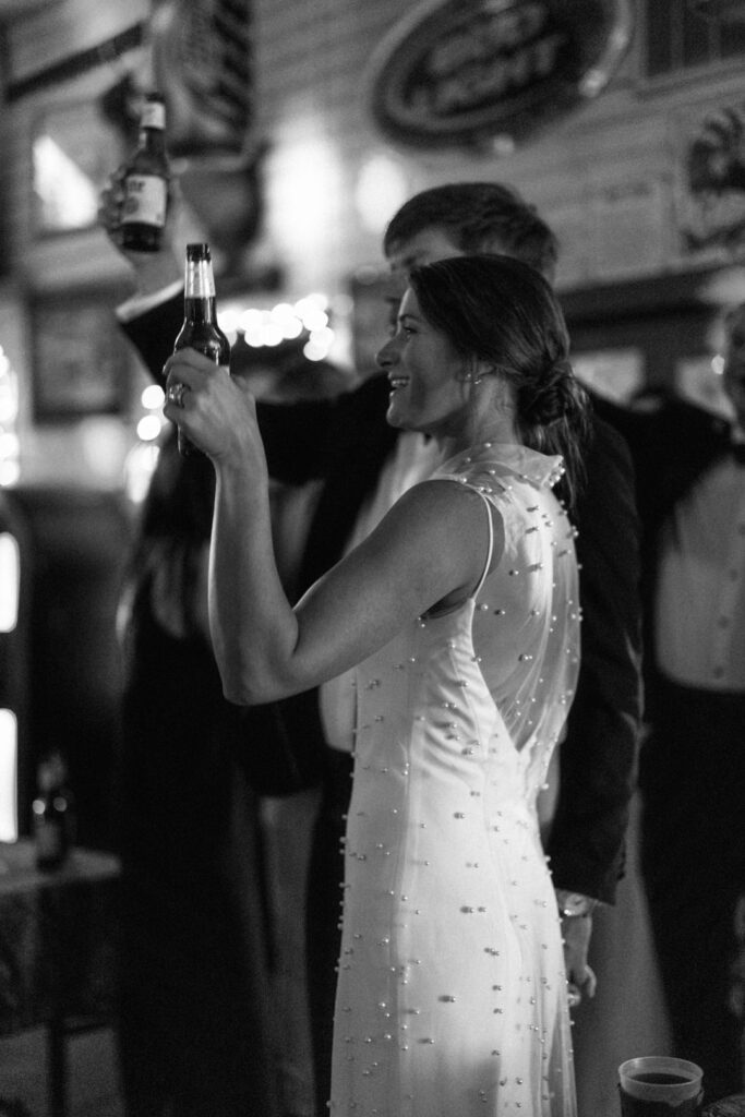 black and white of bride and groom raising beers