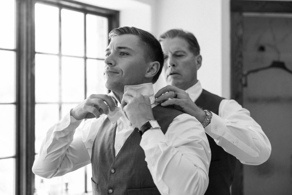 black and white of groom tying bow tie