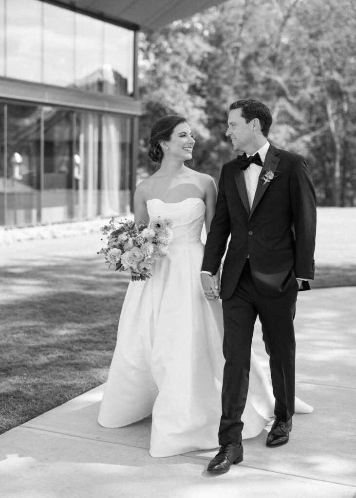 black and white of bride and groom walking holding hands 