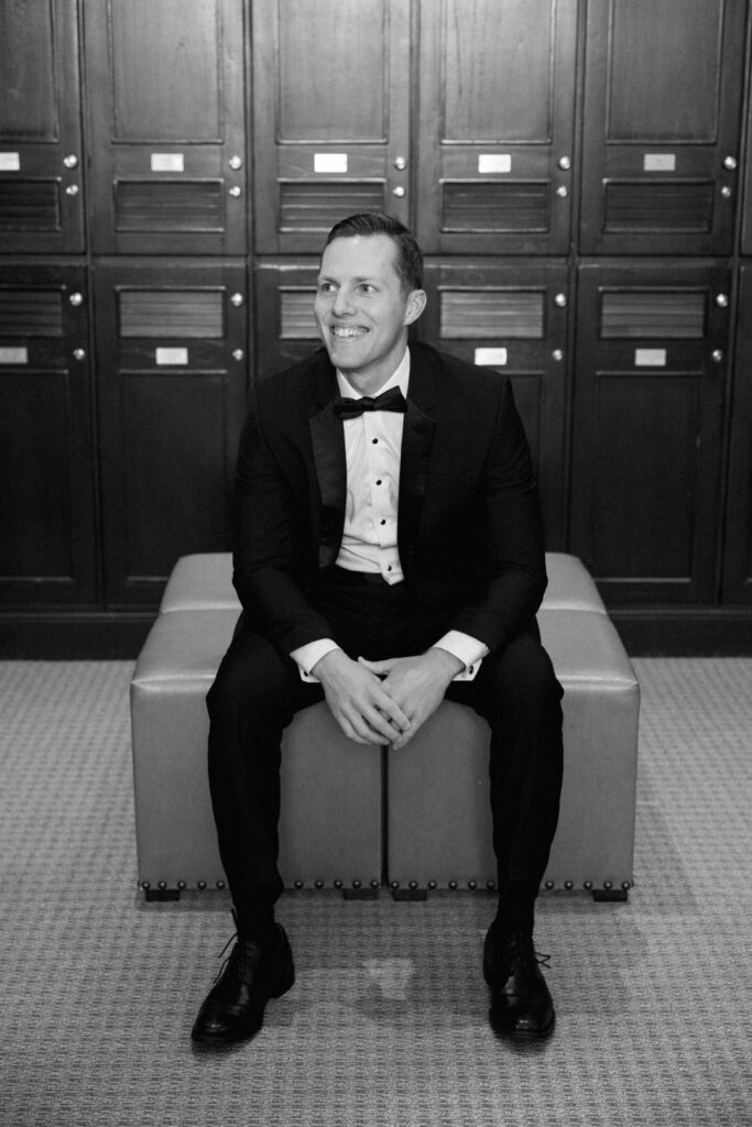 black and white of groom smiling sitting in locker room