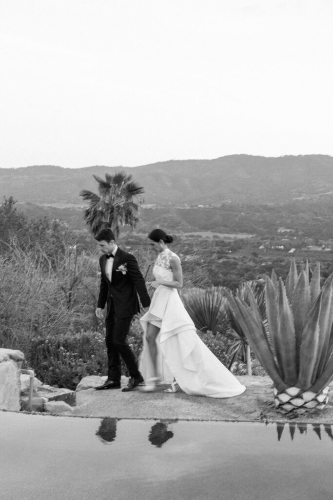 black and white of bride and groom Walking by pool 