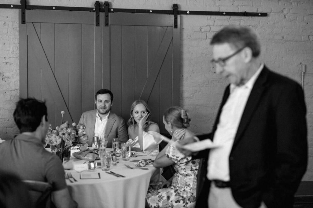 black and white of grooms father giving toast and bride crying