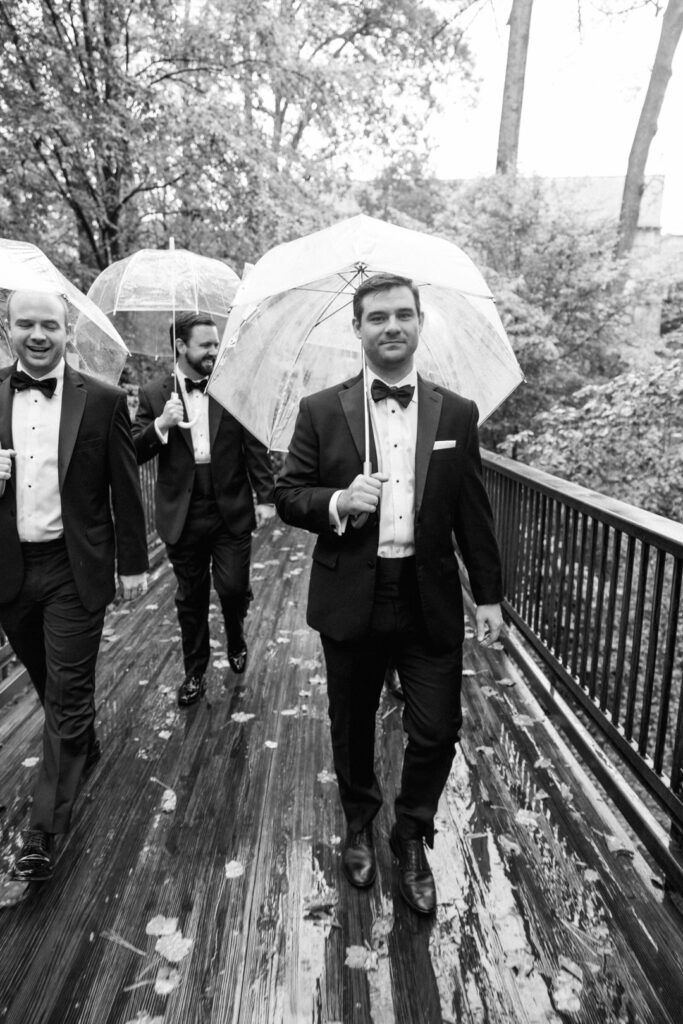 black and white of groomsmen with umbrellas walking through rain