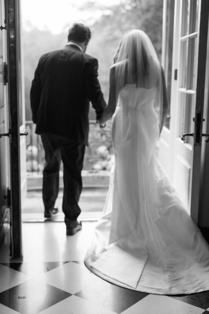 black and white of bride and groom walking out Swan House Doors