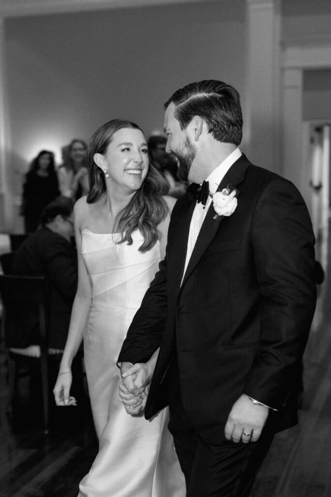 black and white of bride and groom holding hands walking into reception