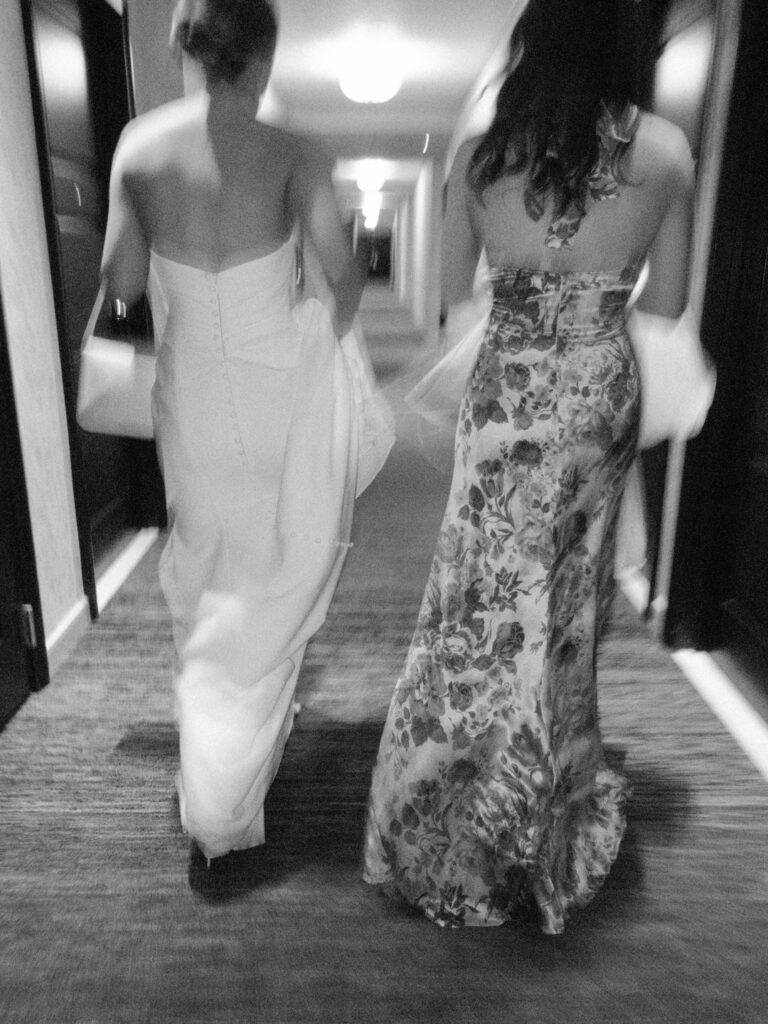 black and white of bride and sister walking down hotel hallway