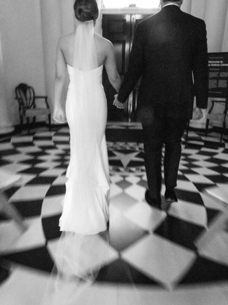 black and white of bride and groom walking holding hands