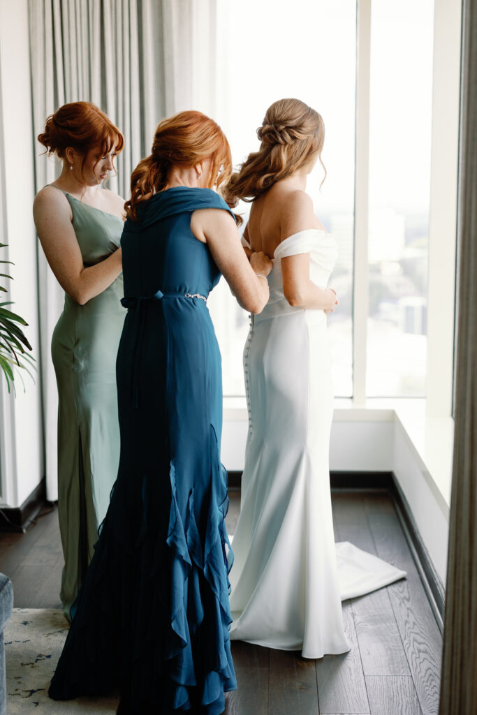 bride getting dressed with mom and sister