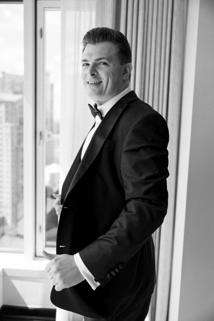 black and white of groom putting on jacket