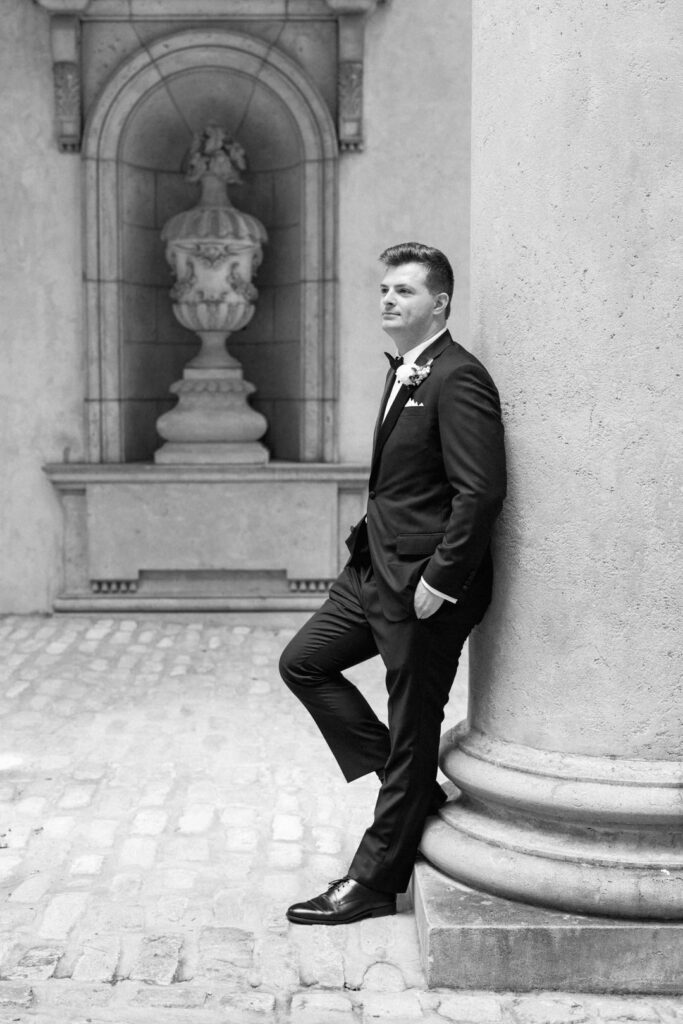 black and white of groom leaning on pillar