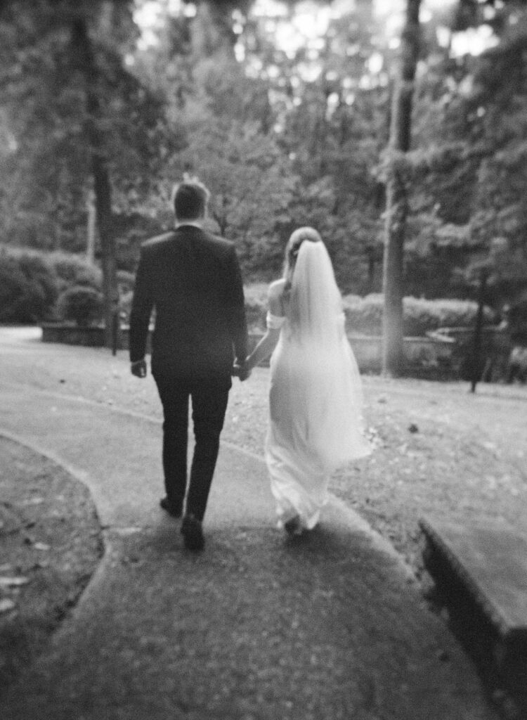 black and white of bride and groom holding hands walking off