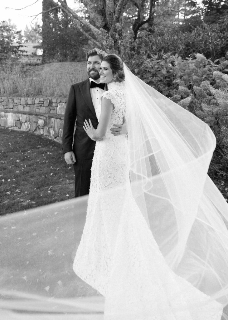 black and white of bride and groom with veil blowing in the wind