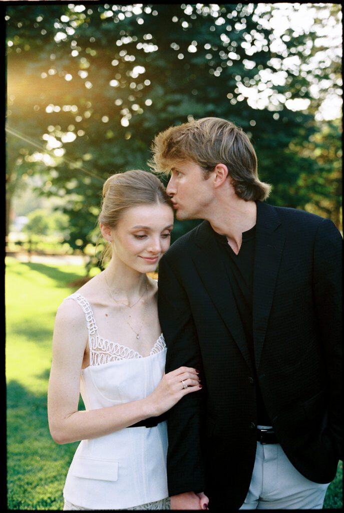 Groom kissing Bride on head with sunlight behind